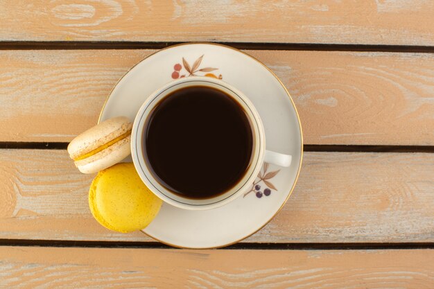 Eine Tasse Kaffee von oben heiß und stark mit französischen Macarons auf dem cremefarbenen rustikalen Schreibtisch trinken Kaffee Foto stark