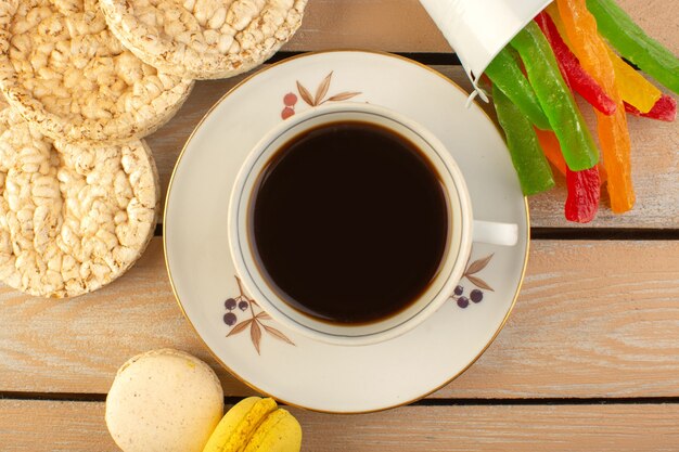 Eine Tasse Kaffee von oben heiß und stark mit französischen Macarons und Marmelade auf dem cremefarbenen rustikalen Schreibtisch trinken Kaffee Foto starke Süßigkeiten