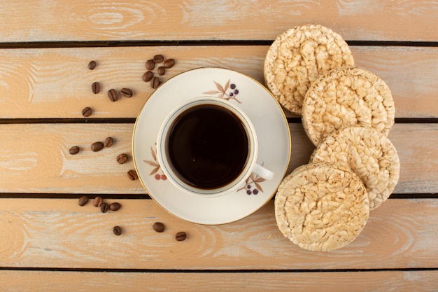 Eine Tasse Kaffee von oben heiß und stark mit frischen braunen Kaffeesamen und Crackern auf dem cremefarbenen rustikalen Schreibtischkaffee-Samengetränk-Fotokorn