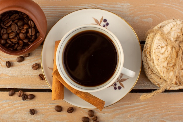 Eine Tasse Kaffee von oben heiß und stark mit frischen braunen Kaffeesamen Zimt und Cracker auf der Creme rustikalen Schreibtisch Kaffeesamen Getränk Fotokorn