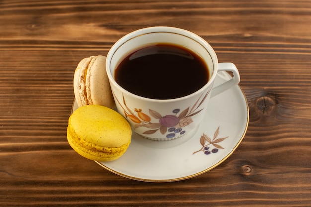 Eine Tasse Kaffee von vorne, heiß und stark mit französischen Macarons auf dem braunen hölzernen rustikalen Schreibtischkaffee-Heißgetränk
