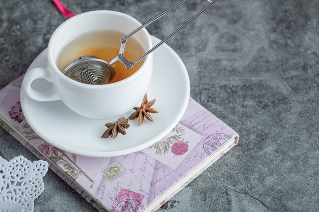 Eine Tasse köstlichen Tee mit Sternanis auf weißem Teller.