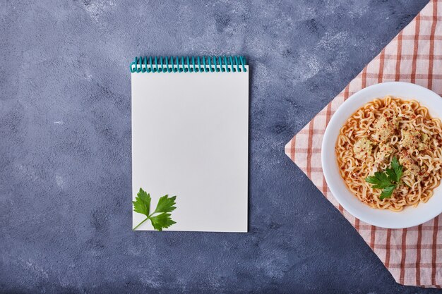 Eine Tasse Spaghetti mit einem Rezeptbuch beiseite.