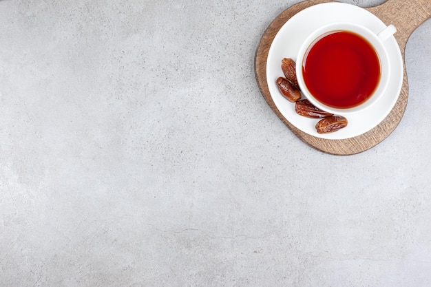 Eine Tasse Tee auf einer Untertasse mit Datteln auf einem Holzbrett, auf Marmorhintergrund. Hochwertiges Foto