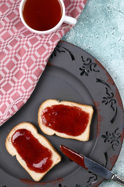 Eine Tasse Tee mit einem Erdbeermarmeladenbrot.