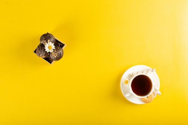 Eine Tasse Tee mit Schokoladenpralinen auf Gelb. Draufsicht