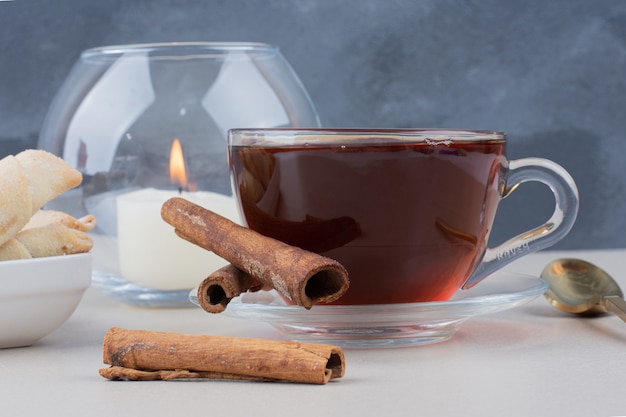 Eine Tasse Tee mit Zimt und Keksen auf weißem Tisch.