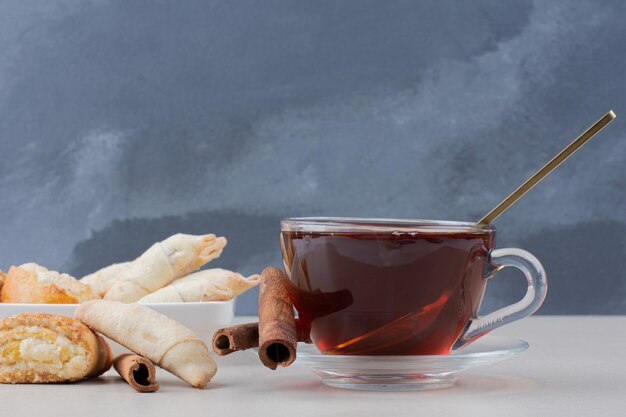 Eine Tasse Tee mit Zimt und Keksen auf weißem Tisch.