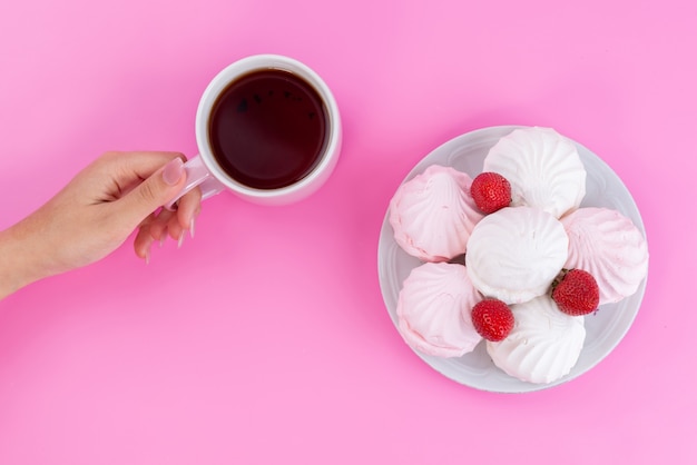 Eine Tasse Tee von oben mit Baisers und Erdbeeren in der Platte auf rosa Tee-Keks-Kuchenfarbe