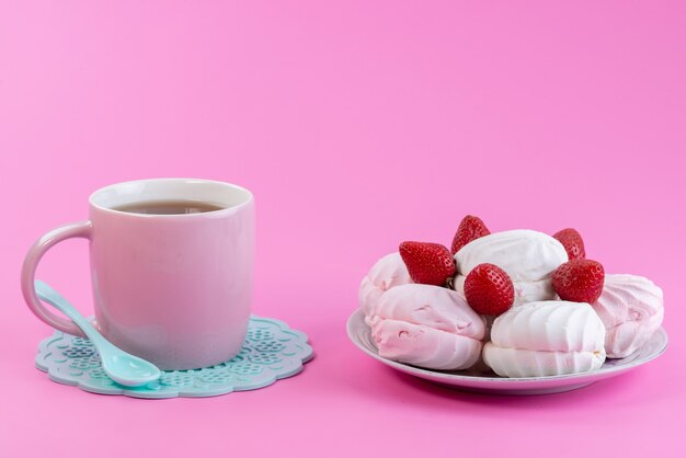 Eine Tasse Tee von vorne mit Weiß, Baiser und frischen Erdbeeren in der Platte auf rosa Teekekskuchen-Süßigkeiten