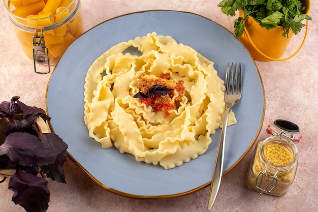 Eine Teigansicht der Draufsicht kochte lecker gesalzenes in der runden blauen Platte mit Blume und rohen Nudeln auf rosa Schreibtisch