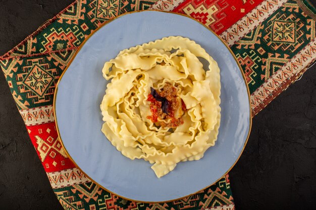 Eine Teignudel von oben, gekocht lecker gesalzen in runder blauer Platte auf entworfenem Teppich und dunklem Schreibtisch