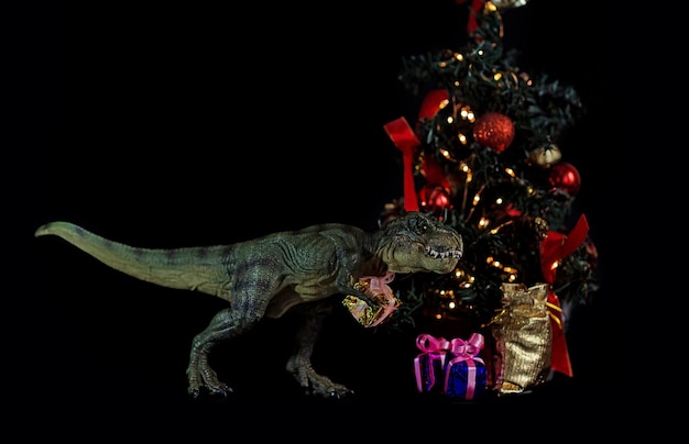 Eine tyrannosaurus spielzeugfigur mit geschenken zu weihnachten und neujahr am weihnachtsbaum auf einem schwarzen