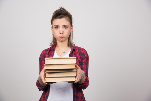 Eine verärgerte Frau, die einen Stapel Bücher an einer grauen Wand zeigt