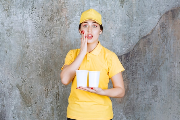 Eine Verkäuferin in gelber Uniform, die zwei Plastikbecher mit Getränken hält und gestresst und verängstigt aussieht