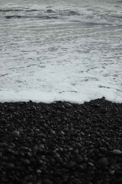 Eine vertikale Graustufenaufnahme von Strandwellen, die am Ufer auftauchen
