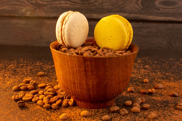 Eine Vorderansicht braune Kaffeesamen innerhalb der braunen Platte mit Macarons auf dem dunklen Körnchengranulat des braunen Kaffeesamens
