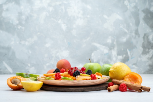 Eine Vorderansicht frisch geschnittene Früchte weich und Vitamin reich an Zimt und ganzen Früchten auf dem hölzernen Schreibtisch und weißen Hintergrundfrüchten Farbfutterfoto