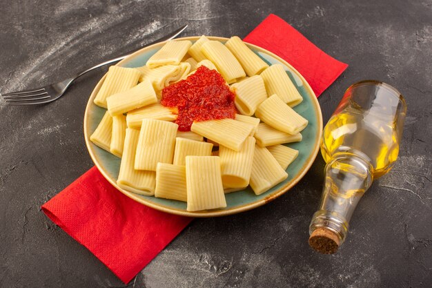 Eine Vorderansicht kochte italienische Nudeln mit Tomatensauce innerhalb Platte auf dem grauen Tischnudeln italienisches Essen Mahlzeit
