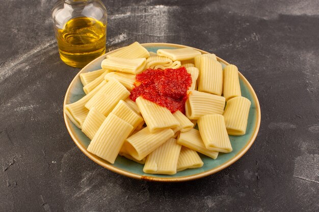 Eine Vorderansicht kochte italienische Nudeln mit Tomatensauce innerhalb Platte auf der grauen Oberfläche