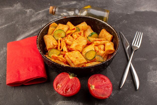 Eine Vorderansicht kochte italienische Nudeln mit Tomatensauce und Gurke in der Pfanne auf der dunklen Oberfläche