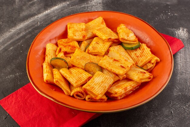 Eine Vorderansicht kochte italienische Nudeln mit Tomatensauce und Gurke innerhalb Platte auf der dunklen Oberfläche