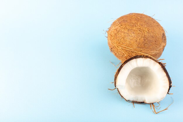 Eine Vorderansicht Kokosnüsse in Scheiben geschnitten und ganz milchig frisch mild isoliert auf dem tropischen exotischen Fruchtnuss des eisblauen Hintergrunds