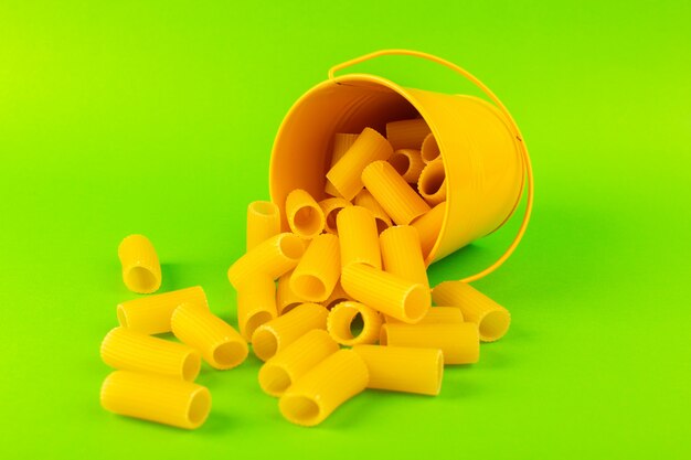 Eine Vorderansicht-Nudeln innerhalb des Korbs bildeten rohen inneren gelben Korb auf dem grünen Hintergrundmahlzeitnahrungsmittel-italienischen Spaghetti