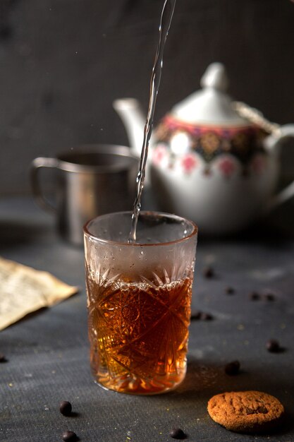 Eine Vorderansicht-Person, die Tee mit gekochtem Wasser zusammen mit Keksen auf dem dunklen Tischkeks-Tee-Kekszucker süß macht