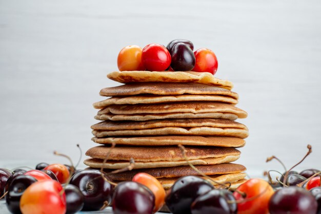 Eine Vorderansicht runde Pfannkuchen gebacken und lecker mit Kirschen auf dem leichten Schreibtisch Kuchen Obst