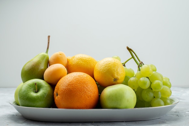 Eine Vorderansicht verschiedener Früchte wie Zitronenbirnen, Äpfel, Trauben und Orangen auf dem weißen Schreibtisch in der Platte Fruchtfarbe Vitamin Sommer frisch