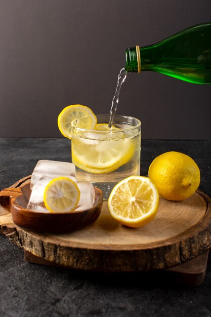 Eine Vorderansicht Wasser mit Zitrone frisch kühles Getränk in Glas mit Eiswürfeln mit geschnittenen Zitronen im Dunkeln gießen