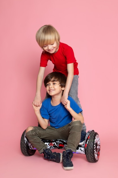 Eine Vorderansicht zwei Jungen entzückenden süßen niedlichen glücklichen reitenden Segway auf dem rosa Boden