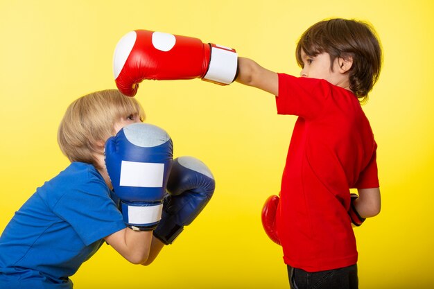 Eine Vorderansicht zweier Jungen, die in Boxhandschuhen an der gelben Wand kämpfen