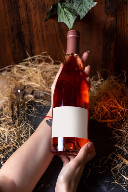 Eine Vorderansichtfrau, die Weinflasche des Weißweins auf dem braunen Hintergrundalkoholtrink-Weingut hält