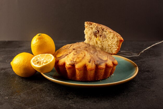 Eine vordere geschlossene Ansicht runder süßer Kuchen köstlicher leckerer Schoko-Kuchen, der in blauen Teller zusammen mit frischen Zitronen im Dunkeln geschnitten wird