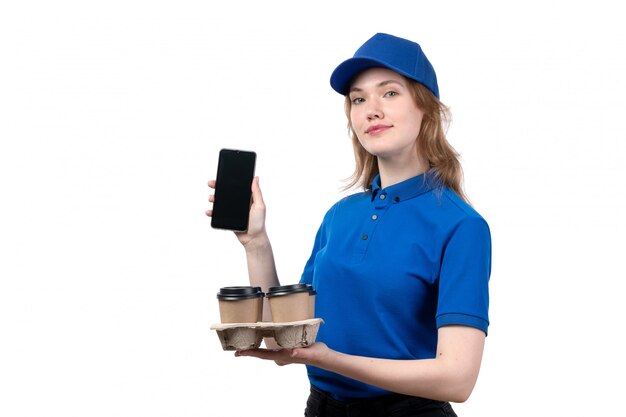 Eine weibliche weibliche Kurierfrau der Vorderansicht des Lebensmittellieferdienstes lächelnd, die Kaffeetassen und Telefon auf Weiß hält