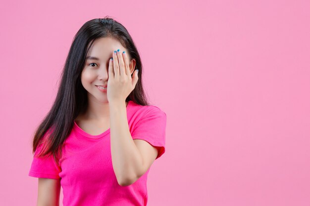 Eine weiße asiatische Frau legt ihre linke Hand auf ihre Augen auf ein Rosa.