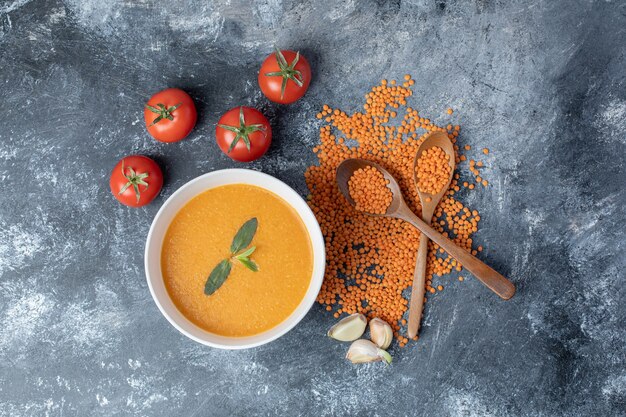 Eine weiße Schüssel Linsensuppe mit Tomaten und Holzlöffeln.