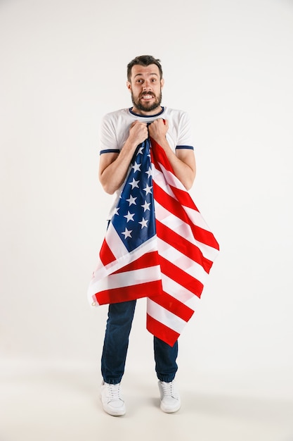 Einen Unabhängigkeitstag feiern. Sternenbanner. Junger Mann mit Flagge der Vereinigten Staaten von Amerika lokalisiert auf weißer Studiowand. Sieht als Patriot seines Landes verrückt glücklich und stolz aus.