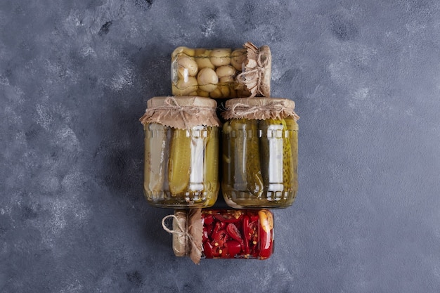 Eingelegte Gurken, Oliven und Paprika in Gläsern auf blauem Grund.
