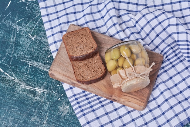 Eingelegte Oliven im Glas mit Schwarzbrotscheiben auf Blau.