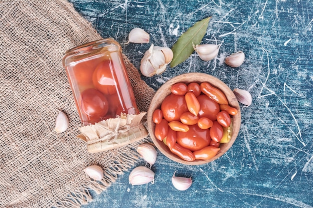 Eingelegte Tomaten im Glas und Schüssel mit Knoblauch auf Blau.