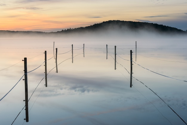 Eingezäuntes Fahrerlager auf einem nebligen See während des Sonnenuntergangs in Radasjon, Schweden