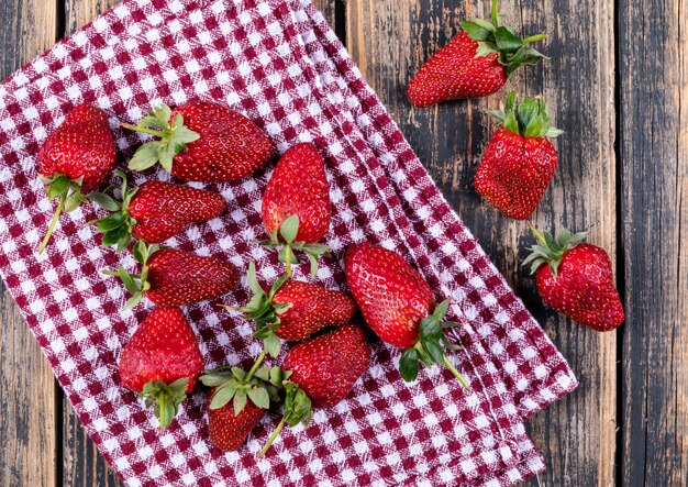 Einige Erdbeeren auf Picknicktuch auf Holztisch, flach liegen.