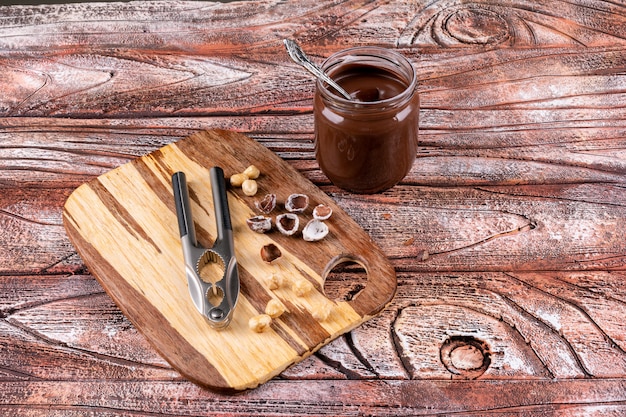 Einige geschälte und gereinigte Haselnüsse mit Kakaostreifen und Nussknackern auf Holztisch, Draufsicht.