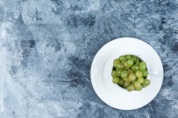 Einige grüne Trauben mit Platte in einer weißen Tasse auf grungy Gipshintergrund, Draufsicht.