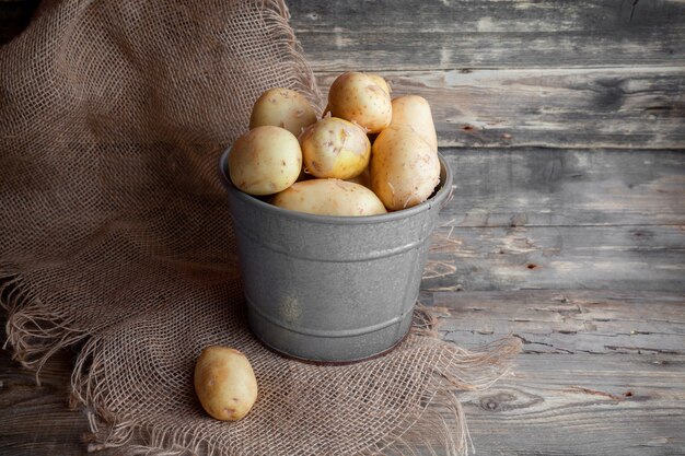 Einige Kartoffeln mit Stoff in einem grauen Eimer auf dunklem hölzernem Hintergrund, Seitenansicht.
