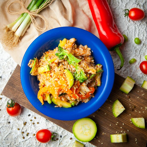 Einige köstliche Mahlzeit mit Frühlingszwiebeln und Pfeffer in einem blauen Teller auf Holz, rotem Stoff und weißem strukturiertem Hintergrund, Draufsicht.