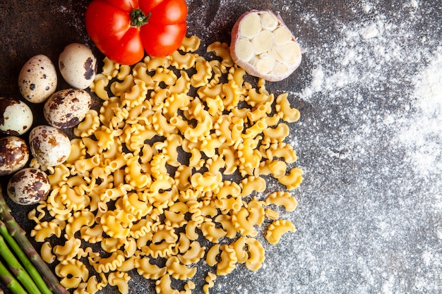 Einige Makkaroni mit Eiern, Tomate und Knoblauch auf dunklem strukturiertem Hintergrund, Draufsicht.